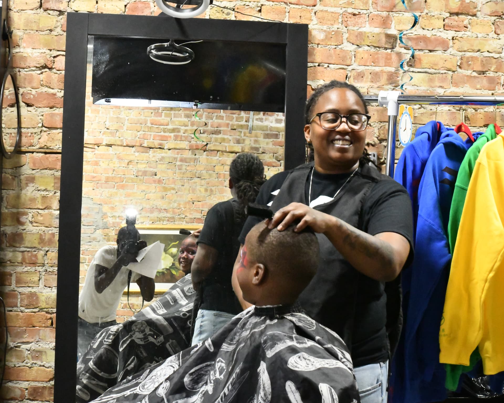 Moe the BarbHer smiling while giving a young boy a fresh haircut in the shop