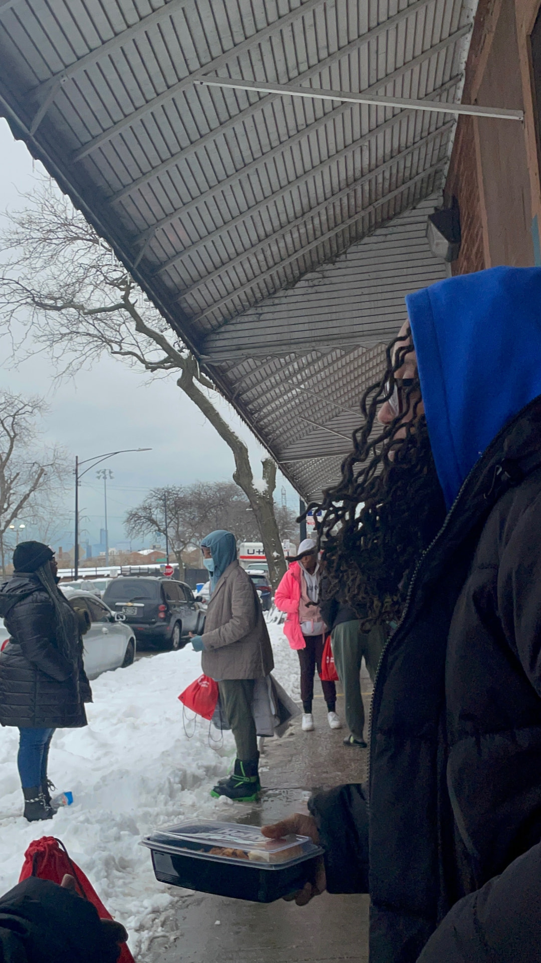 Neighbors receiving hot meals and red care bags on a snowy sidewalk