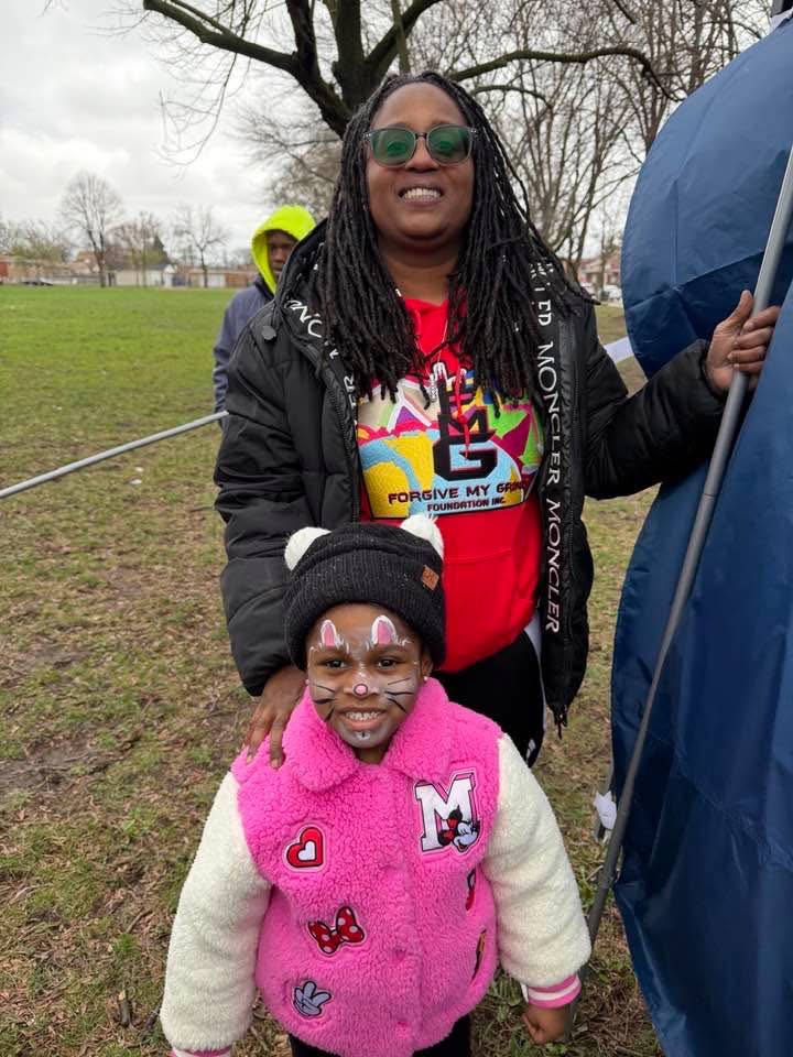 A smiling volunteer with a young girl in face paint at a park event